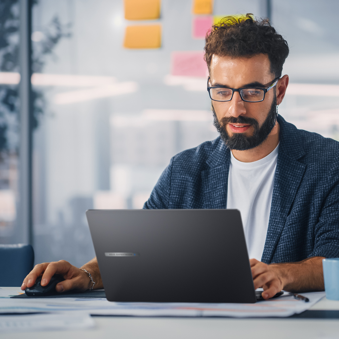 一位男性员工坐在桌前使用并看着 ASUS ExpertBook B 系列笔记本电脑